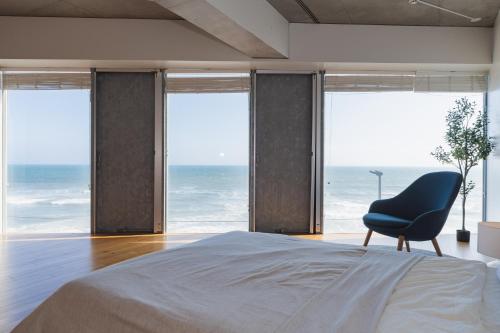 a bedroom with a bed and a chair in front of the ocean at 湘南OCEAN HOUSE in Koshigoe