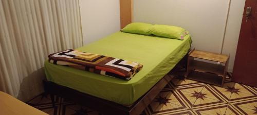 um pequeno quarto com uma cama com lençóis verdes em Travelershouse Casa Hospedaje em Huanchaco