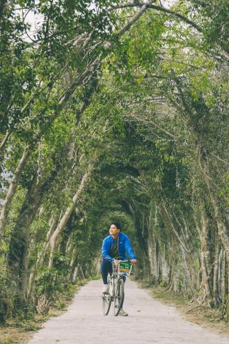 a man riding a bike down a path with trees at Thung Nham Resort in Ninh Binh