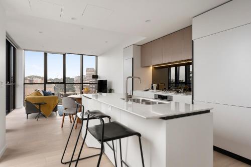 Urban Rest North Sydney Apartments في سيدني: مطبخ به كونترات بيضاء وكراسي وقمه منضده
