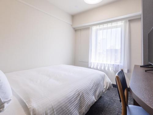 a white bedroom with a bed and a desk and a window at Hotel Wing International Shizuoka in Shizuoka
