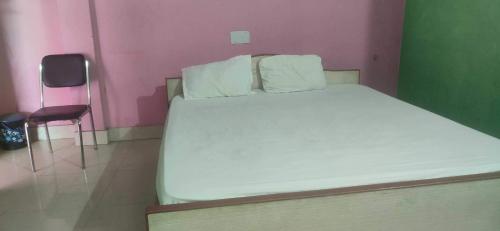 Cama blanca en habitación rosa con silla en OYO Hotel Krishna Internation, en Muzaffarpur