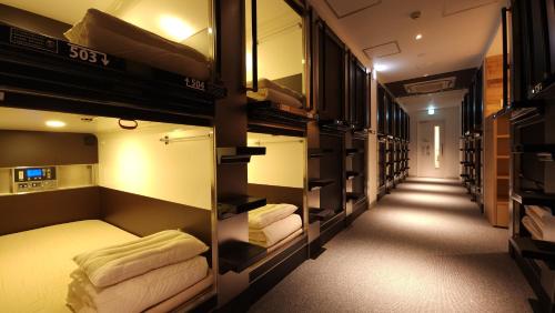 a room with several bunk beds and a hallway at Acro Capsule Hotel Namba Dotonbori in Osaka