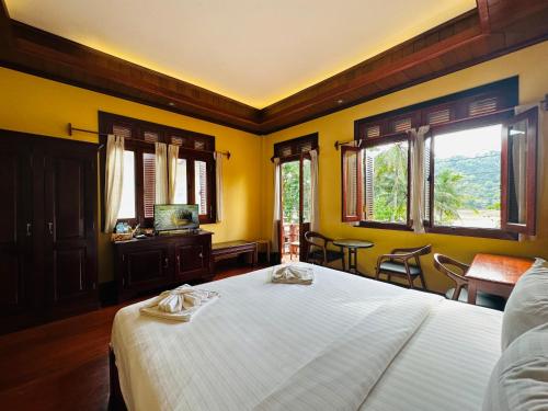 a bedroom with a large bed with yellow walls and windows at Villa Phonethip Mekong Riverside in Luang Prabang