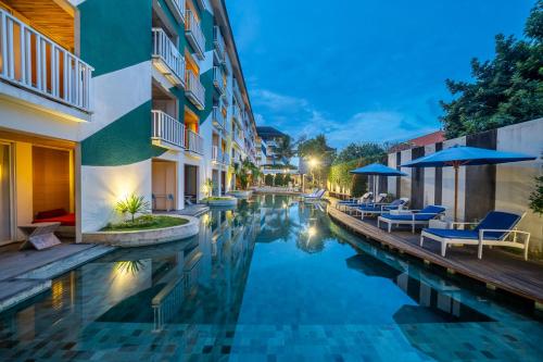 een zwembad met stoelen en parasols naast een gebouw bij Bliss Surfer Hotel by Tritama Hospitality in Legian