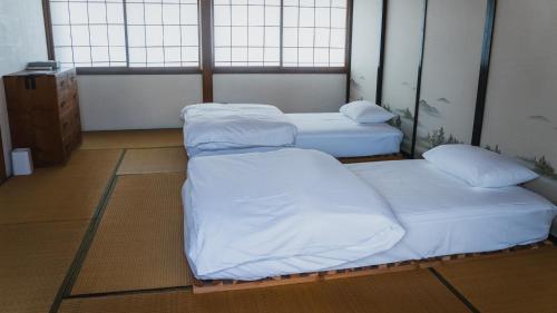 a room with three beds with white sheets and pillows at ゲストハウス麓〼-Rokumasu in Yokooka