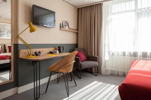 a hotel room with a desk and a bed and a tv at Two Brothers Noordwijk Beach in Noordwijk aan Zee