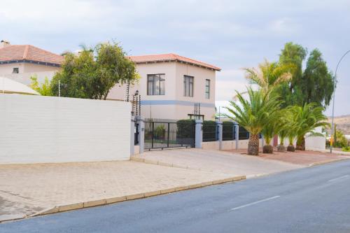 a house on a street with a white fence and trees at L. A. P Guesthouse in Windhoek