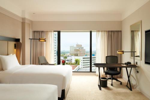 a hotel room with a bed and a desk and a window at Hilton Kuching Hotel in Kuching