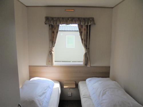 Duas camas num pequeno quarto com uma janela em Kingfisher : Horizon II:- 8 Berth, Close to site entrance em Ingoldmells