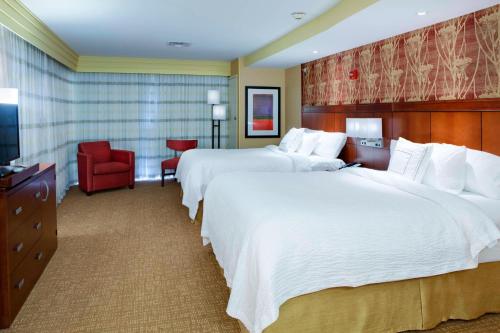 a hotel room with two beds and a red chair at Courtyard by Marriott Indianapolis Noblesville in Noblesville