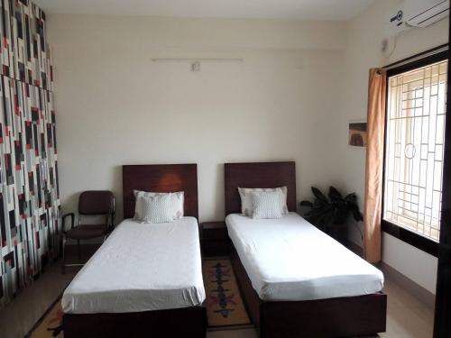 a room with two beds and a chair and a window at Sublime Homestay in Bhubaneshwar