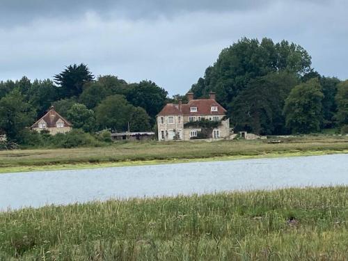 an old house in a field next to a lake at Pretty coastal victorian cottage in Yarmouth IOW in Yarmouth