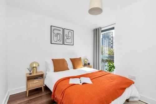 a white bedroom with an orange bed and a window at MODERN LUXE APT just 10 MINS from TOWER BRIDGE! EASY ACCESS TO TUBE AND BUS in London