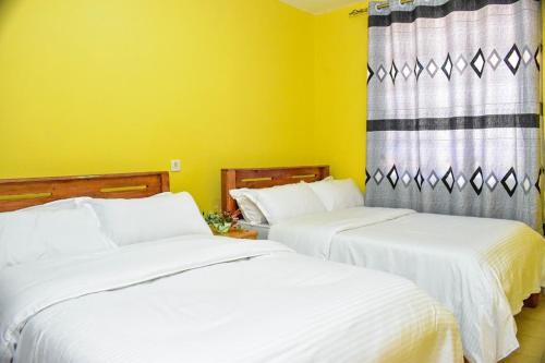 2 weiße Betten in einem Zimmer mit gelben Wänden in der Unterkunft Four seventy in Meru