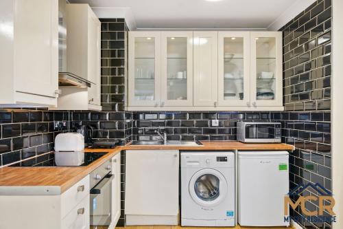 eine Küche mit weißen Schränken, einer Waschmaschine und einem Trockner in der Unterkunft The Sherborne Residence in London