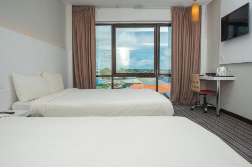 a hotel room with two beds and a desk and a window at Capital O 90083 Riverfront Inn in Bintulu