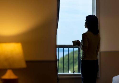a woman standing in front of a window holding a cup at GLAMDAY PORT in Atami