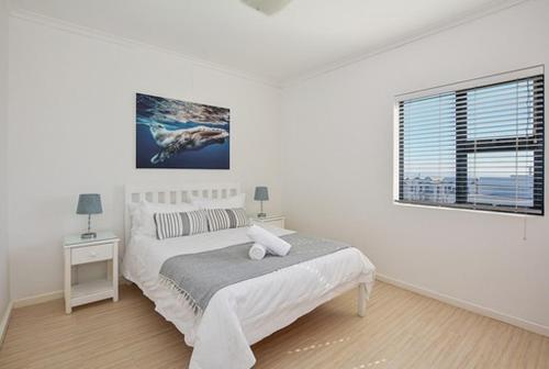 a white bedroom with a bed and a window at Luxury Beachfront Apartment in Big Bay- 2 bedroom in Bloubergstrand