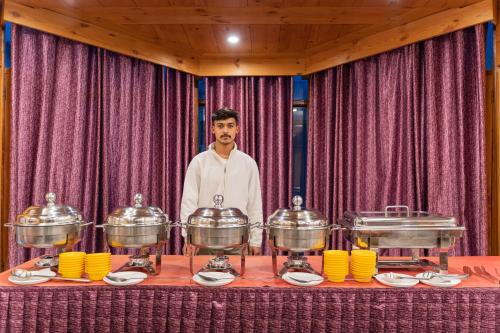 a man standing behind a table with pots and pans at THE CONIFER in Manāli