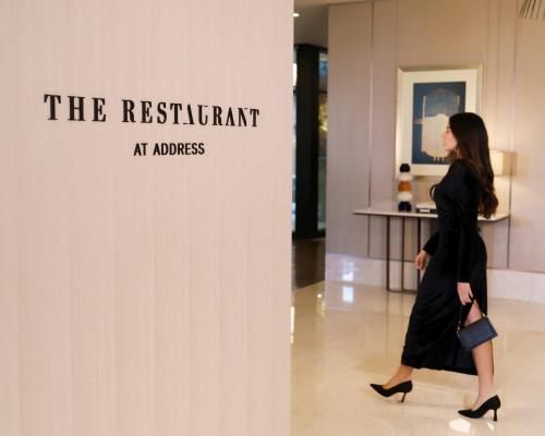 a woman walking past a wall with a sign that reads the restaurant at arousal at Address Istanbul in Istanbul