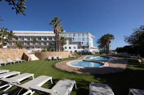 a resort with a pool and lounge chairs and a building at Catalonia Mirador des Port in Mahón