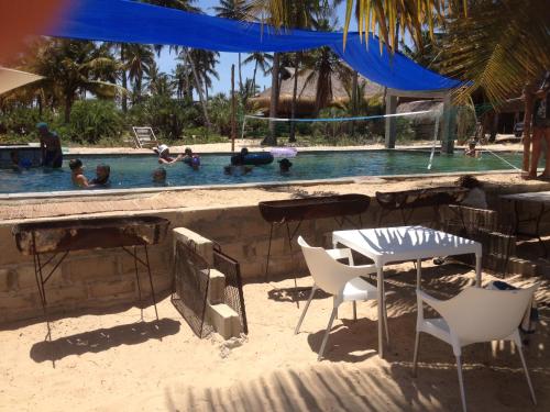 einen Tisch und Stühle im Sand in der Nähe eines Pools in der Unterkunft Barra Dica - CAMPING in Inhambane
