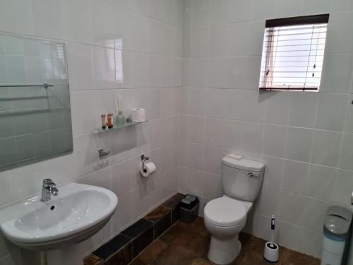 a white bathroom with a toilet and a sink at The Green Lizard Guesthouse in Nelspruit