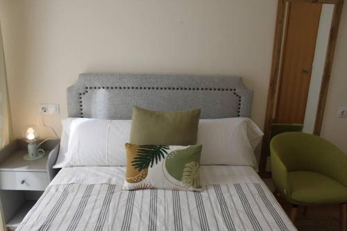 a bedroom with a bed with two pillows and a green chair at Apartamento Turístico HB in Villafranca