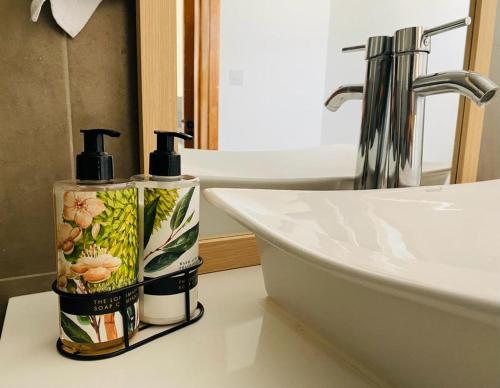 een badkamer met twee flessen geurstoffen naast een wastafel bij Into the Sun - Modern Holiday Home in Albion