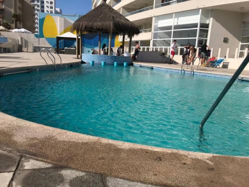 a large blue swimming pool with a straw umbrella at Sobre línea de Playa, Maravillosa Vista al mar 2B/2B-Wifi-TV70´Netf- Estacionamiento propio in La Serena