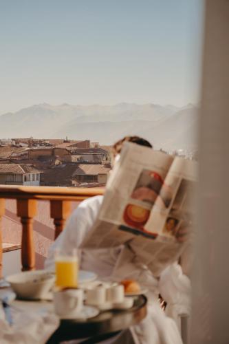 a person reading a newspaper with a plate of food at Palacio Nazarenas, A Belmond Hotel, Cusco in Cusco