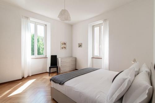 a white bedroom with a bed and two windows at Giuka Apartment by Quokka 360 - close to the station in Massagno