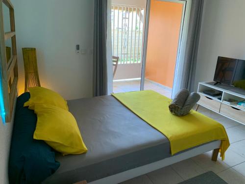 a bedroom with a bed with a yellow blanket and a television at Le nid du Kikiwi , refuge relaxant avec jardin in Cayenne