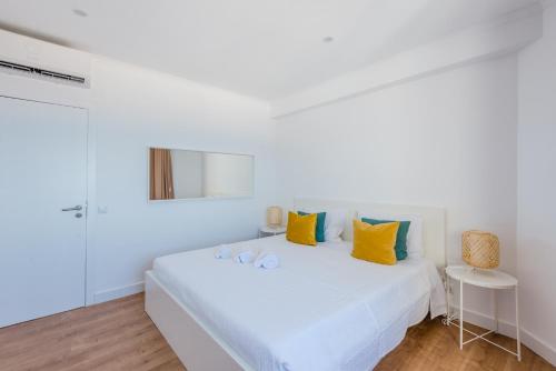 a white bedroom with a white bed with yellow and green pillows at Vista Mar in Quarteira