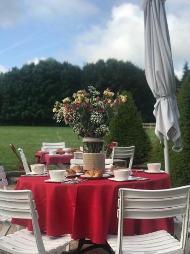 a table with a red table cloth and a vase with flowers at Domaine de L'orangerie du château de Motteville chambres d'hotes in Motteville