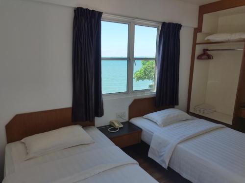 a bedroom with two beds and a window with the ocean at Marine Bay Hotel in Sandakan
