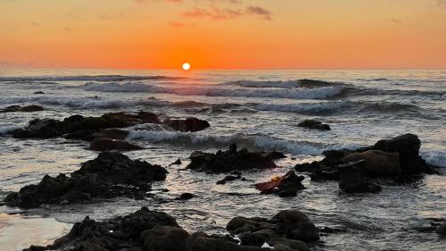 - un coucher de soleil sur l'océan avec des vagues et des rochers dans l'établissement Club Evasion, à Tamelalt