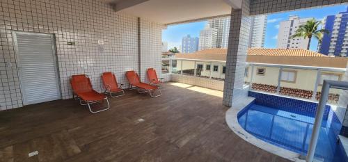 a room with a swimming pool and red chairs at Lindo apto com piscina em Praia Grande - QX01H in Solemar