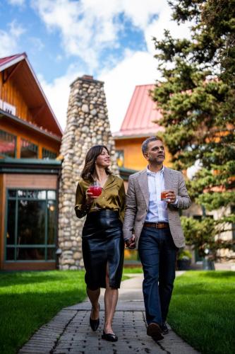 a man and a woman walking down a sidewalk with drinks at Post Hotel & Spa in Lake Louise