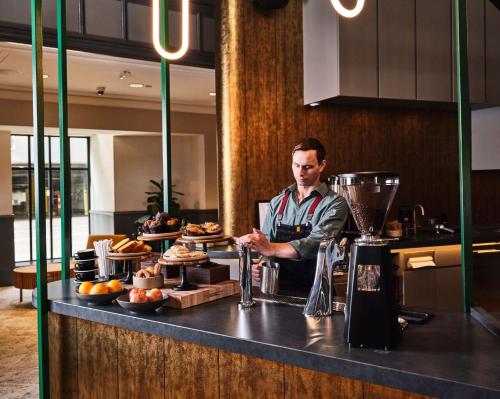 a man standing behind a counter with food at Joinery Hotel Pittsburgh, Curio Collection by Hilton in Pittsburgh