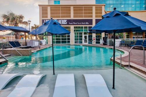 a swimming pool with blue umbrellas in front of a building at Hilton Garden Inn Virginia Beach Oceanfront in Virginia Beach