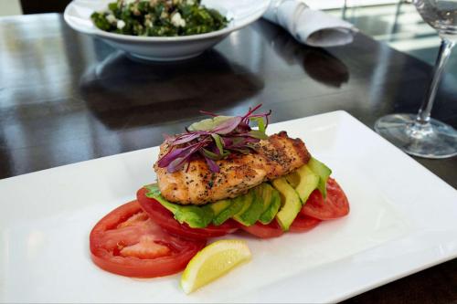 a white plate with a fish sandwich with tomatoes and a salad at DoubleTree by Hilton San Francisco Airport North Bayfront in Brisbane