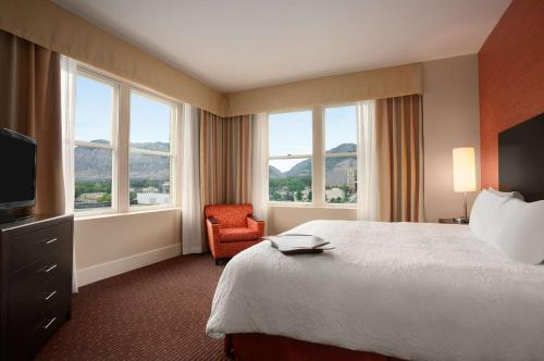 a hotel room with a bed and a chair and windows at Hampton Inn and Suites Ogden in Ogden