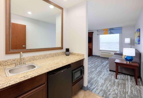 Hampton Inn & Suites Dallas-Arlington-South في أرلينغتون: حمام مع حوض ومرآة وغرفة معيشة