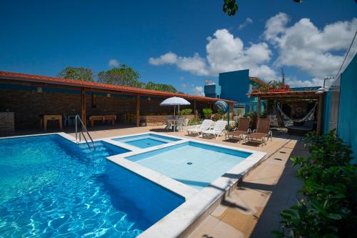 ein Swimmingpool neben einer Terrasse mit Stühlen und einem Sonnenschirm in der Unterkunft Pousada Vovó Zilda Maragogi in Maragogi