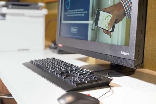 a person holding a cell phone in front of a computer monitor at Hampton Inn Arvin Tejon Ranch, Ca in Wheeler Ridge