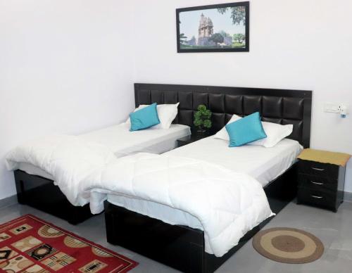 a bedroom with two beds with white and blue pillows at Khajuraho Glory Homestay in Khajurāho