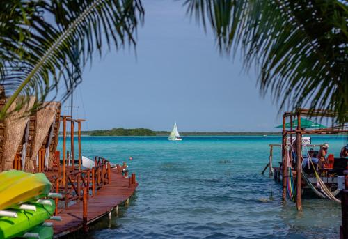 a boat on the water with a sailboat in the distance at El Búho Lagoon Bacalar in Bacalar