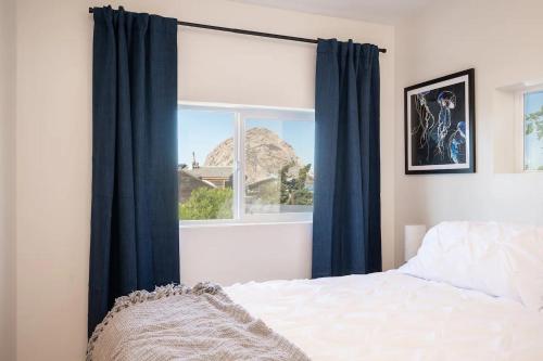 Morro Bay Vacation Rentals في مورو باي: غرفة نوم مع نافذة مع ستائر زرقاء وسرير